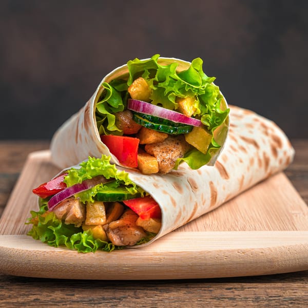 Two T3END shawarma wraps filled with chicken, lettuce, red onion, cucumber, and red peppers on a wooden board.