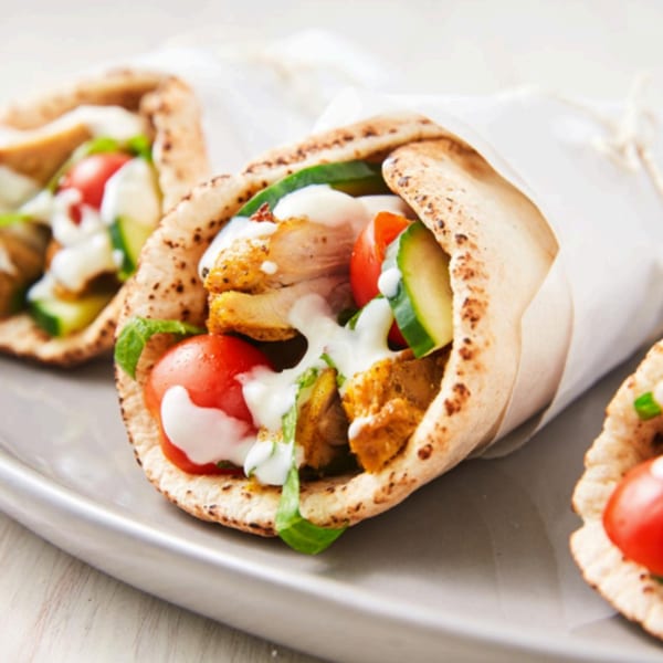 Three T3END shawarma wraps with chicken, tomatoes, cucumbers, and white sauce on a gray plate.