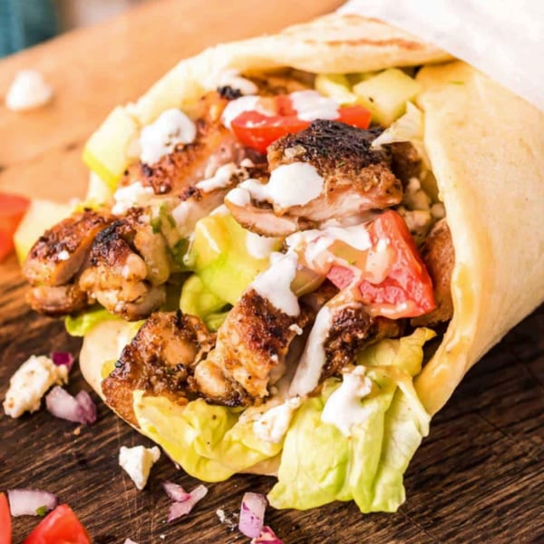 A T3END shawarma wrap filled with grilled chicken, lettuce, tomatoes, and white sauce on a wooden board.