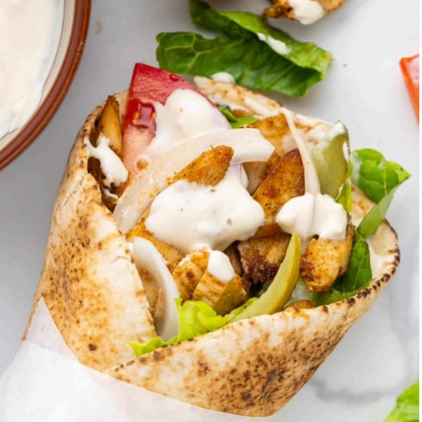T3END shawarma with chicken, lettuce, tomatoes, onions, pickles, and white sauce in pita bread.