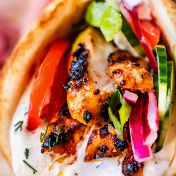 Close-up of a T3END chicken shawarma with charred chicken, white sauce, tomatoes, and cucumbers.