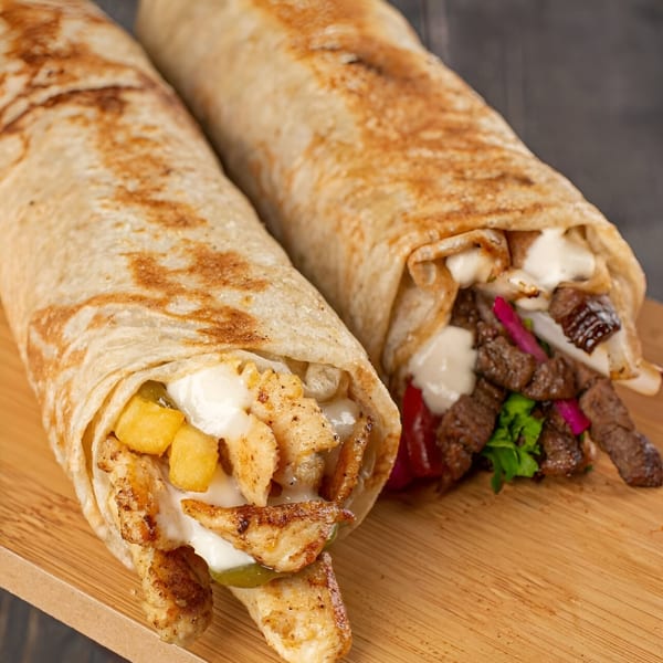 Two T3END shawarmas, one chicken and one beef, with sauces and fillings on a wooden board.