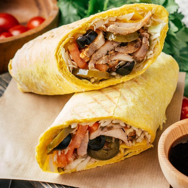 Two T3END shawarmas, sliced open to reveal chicken, olives, pickles, and tomatoes, on brown paper.